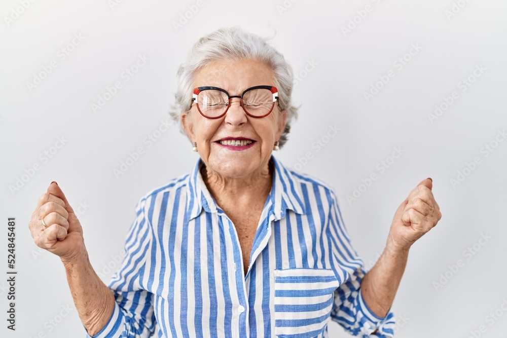 Senior woman with grey hair standing over white background celebrating mad and crazy for success with arms raised and closed eyes screaming excited. winner concept Senior woman with grey hair standing over white background celebrating mad and crazy for success with arms raised and closed eyes screaming excited. winner concept