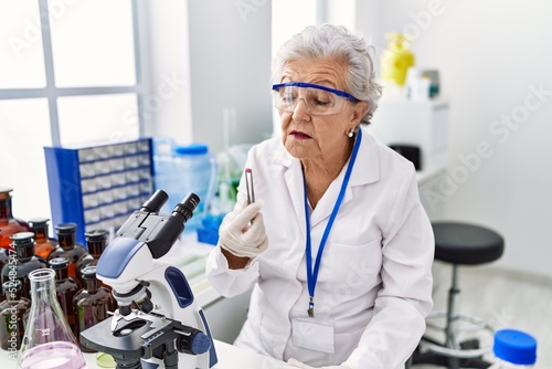 Senior grey-haired woman wearing scientist uniform holding pill at laboratory