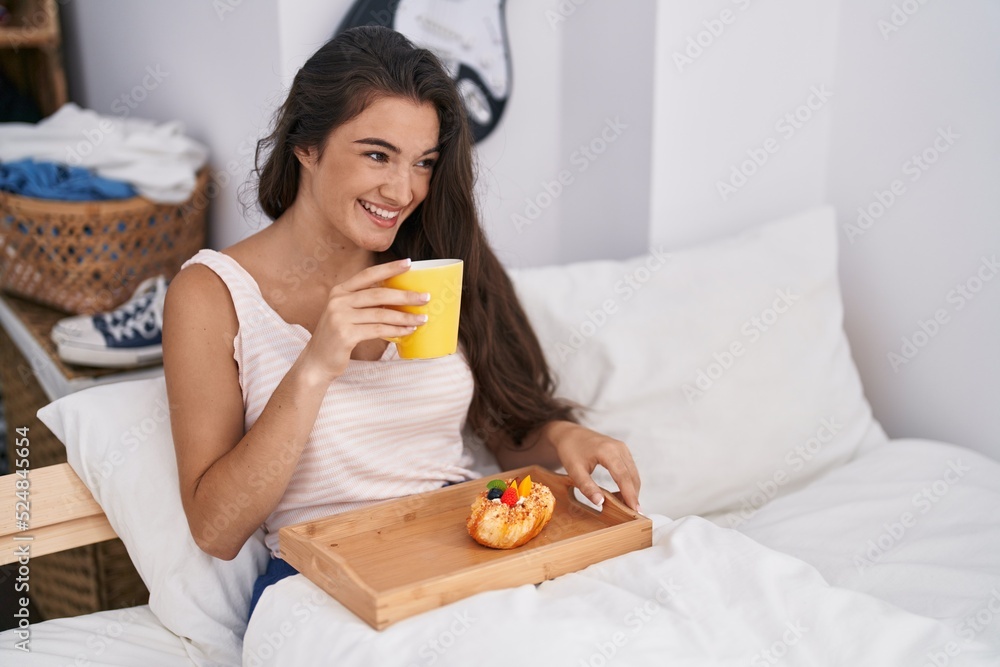 Young hispanic woman having breakfast sitting on bed at bedroom