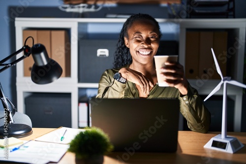 African woman working using computer laptop at night winking looking at the camera with sexy expression, cheerful and happy face.