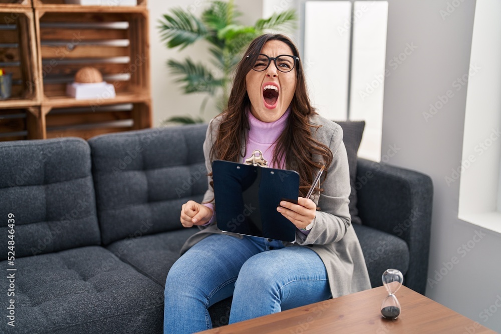 Young brunette woman working at consultation office angry and mad screaming frustrated and furious, shouting with anger. rage and aggressive concept. Young brunette woman working at consultation office angry and mad screaming frustrated and furious, shouting with anger. rage and aggressive concept.