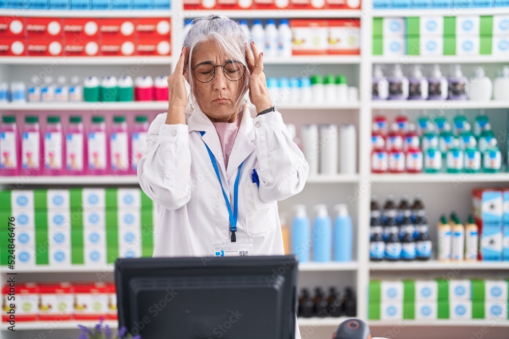 Middle age woman with tattoos working at pharmacy drugstore with hand on head, headache because stress. suffering migraine. Middle age woman with tattoos working at pharmacy drugstore with hand on head, headache because stress. suffering migraine.