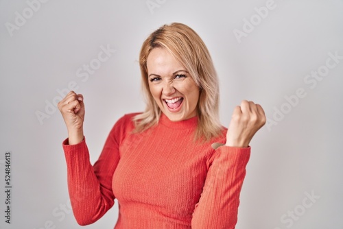 Blonde woman standing over isolated background very happy and excited doing winner gesture with arms raised, smiling and screaming for success. celebration concept.