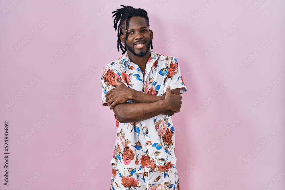 African man with dreadlocks wearing summer shirt over pink background happy face smiling with crossed arms looking at the camera. positive person. African man with dreadlocks wearing summer shirt over pink background happy face smiling with crossed arms looking at the camera. positive person.
