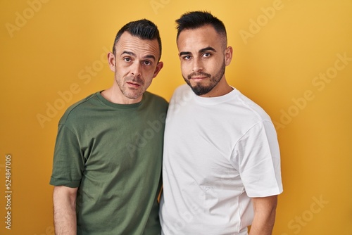 Homosexual couple standing over yellow background looking sleepy and tired, exhausted for fatigue and hangover, lazy eyes in the morning.