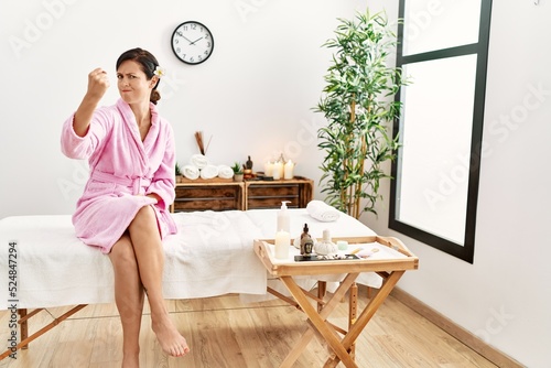 Beautiful caucasian woman wearing bathrobe at wellness spa angry and mad raising fist frustrated and furious while shouting with anger. rage and aggressive concept.