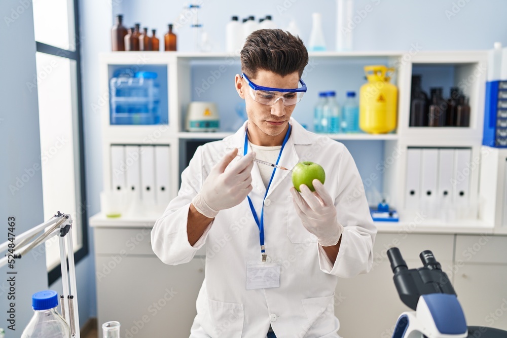 Young hispanic man wearing scientist uniform injecting on apple at laboratory Young hispanic man wearing scientist uniform injecting on apple at laboratory