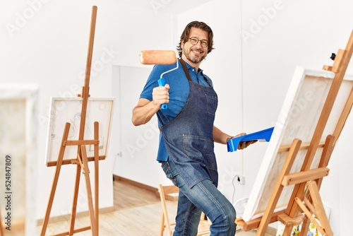 Middle age caucasian man smiling confident drawing using paint roller at art studio