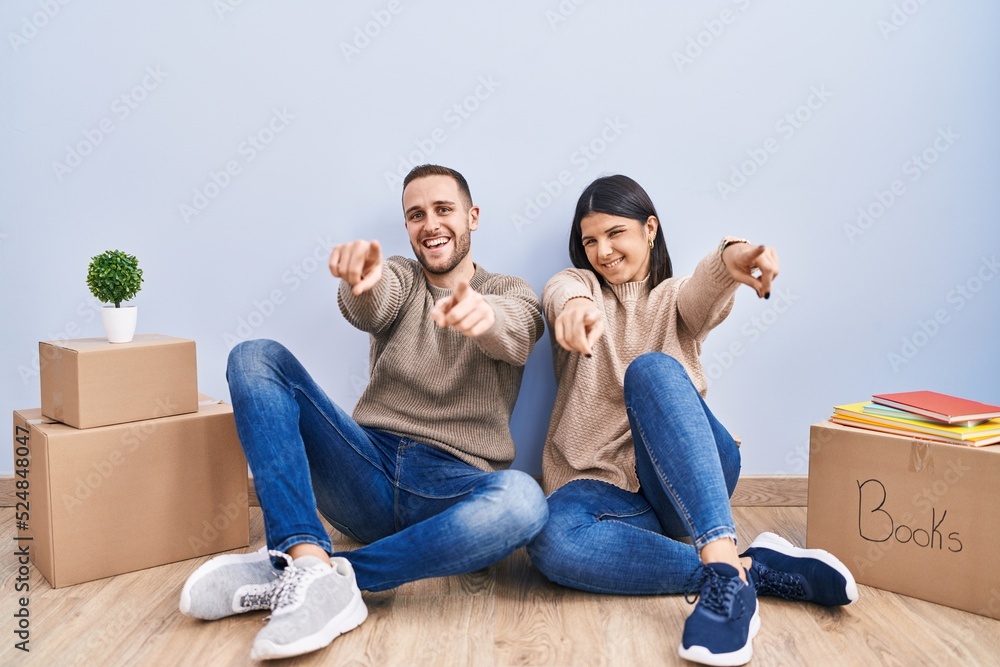 Young couple moving to a new home pointing to you and the camera with fingers, smiling positive and cheerful Young couple moving to a new home pointing to you and the camera with fingers, smiling positive and cheerful