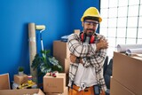 Young hispanic man with beard working at home renovation hugging oneself happy and positive, smiling confident. self love and self care