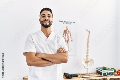 Young arab man wearing physiotherapist uniform standing with arms crossed gesture at clinic photo
