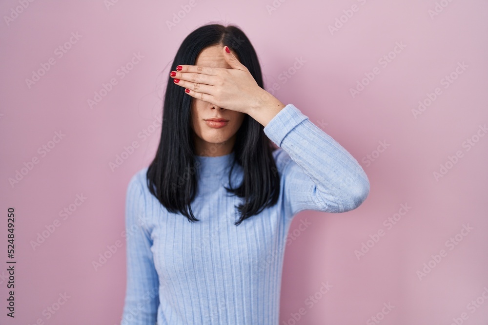 Hispanic woman standing over pink background covering eyes with hand, looking serious and sad. sightless, hiding and rejection concept Hispanic woman standing over pink background covering eyes with hand, looking serious and sad. sightless, hiding and rejection concept