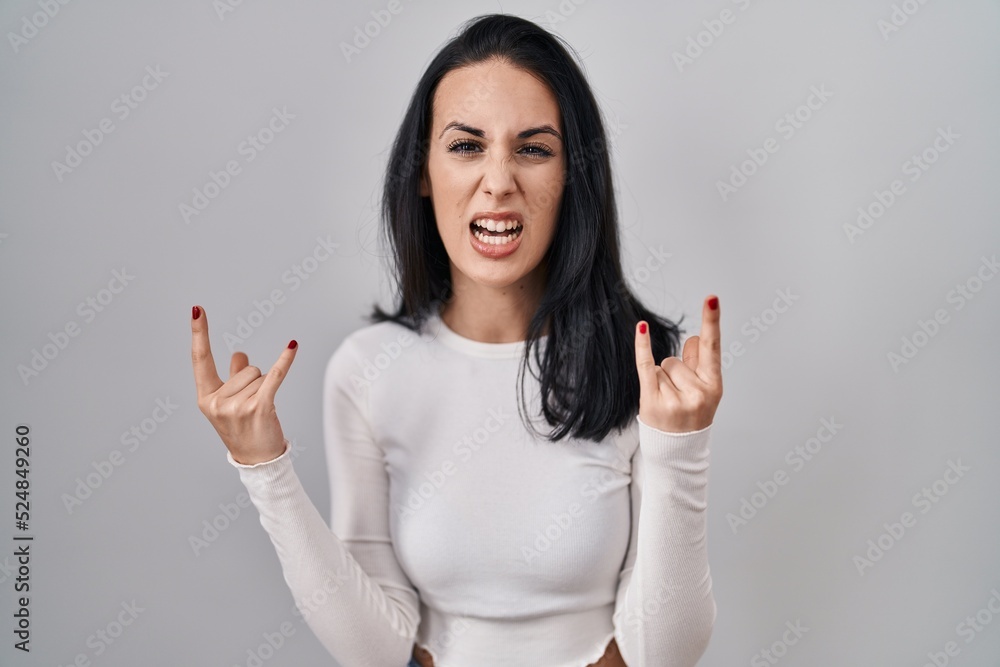 Hispanic woman standing over isolated background shouting with crazy expression doing rock symbol with hands up. music star. heavy concept. Hispanic woman standing over isolated background shouting with crazy expression doing rock symbol with hands up. music star. heavy concept.
