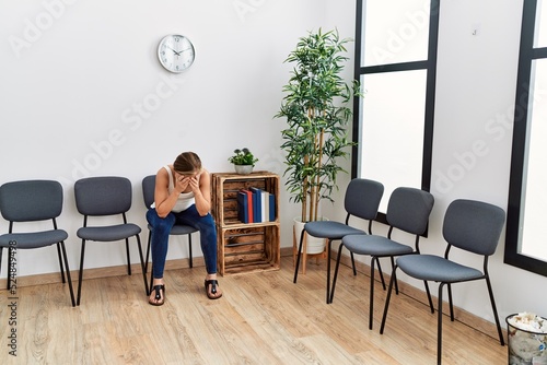 Young caucasian woman desperate with hands on head sitting on chair at waiting room