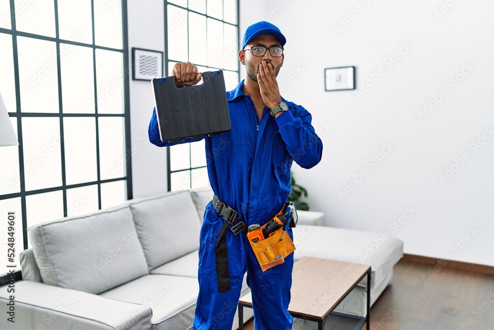 Young indian technician holding toolbox and screwdriver at house covering mouth with hand, shocked and afraid for mistake. surprised expression Young indian technician holding toolbox and screwdriver at house covering mouth with hand, shocked and afraid for mistake. surprised expression