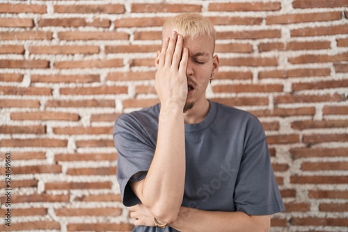 Young caucasian man standing over bricks wall yawning tired covering half face, eye and mouth with hand. face hurts in pain.