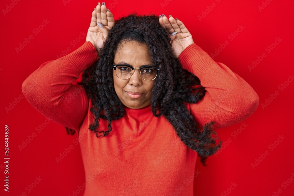 Plus size hispanic woman standing over red background doing bunny ears gesture with hands palms looking cynical and skeptical. easter rabbit concept. Plus size hispanic woman standing over red background doing bunny ears gesture with hands palms looking cynical and skeptical. easter rabbit concept.
