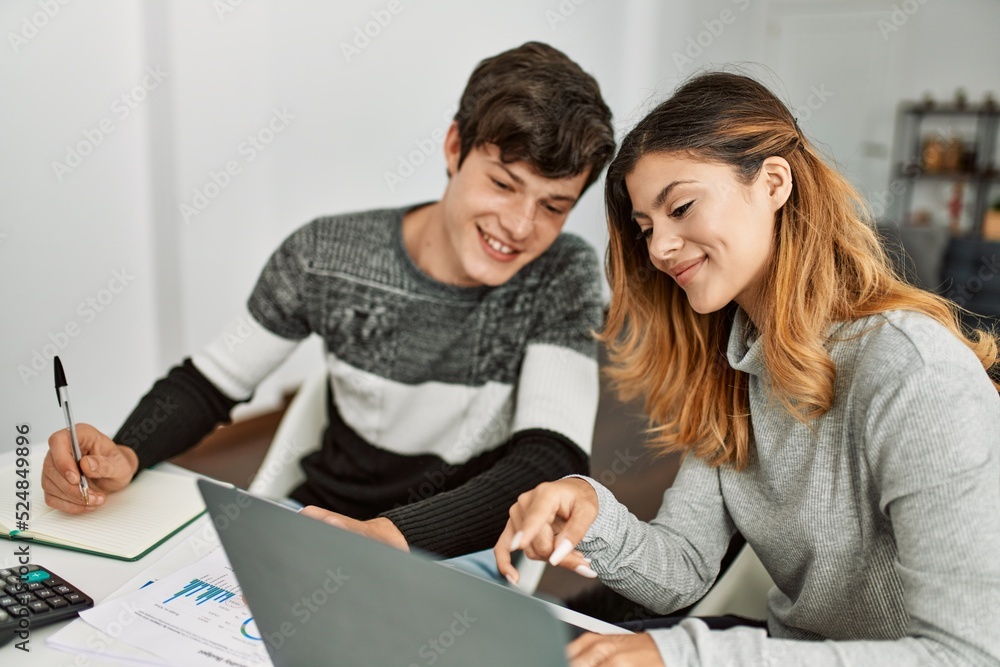 Young couple smiling happy working using laptop sitting on the table at home. Young couple smiling happy working using laptop sitting on the table at home.