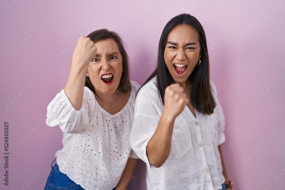 Hispanic mother and daughter together angry and mad raising fist frustrated and furious while shouting with anger. rage and aggressive concept. Hispanic mother and daughter together angry and mad raising fist frustrated and furious while shouting with anger. rage and aggressive concept.