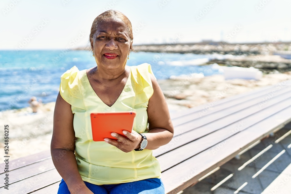 Senior african american woman using touchpad sitting on the bench at ...
