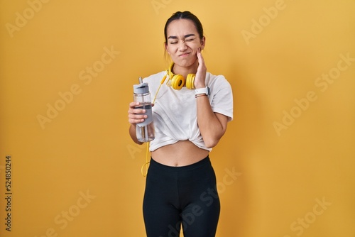 Young south asian woman wearing sportswear drinking water touching mouth with hand with painful expression because of toothache or dental illness on teeth. dentist concept.