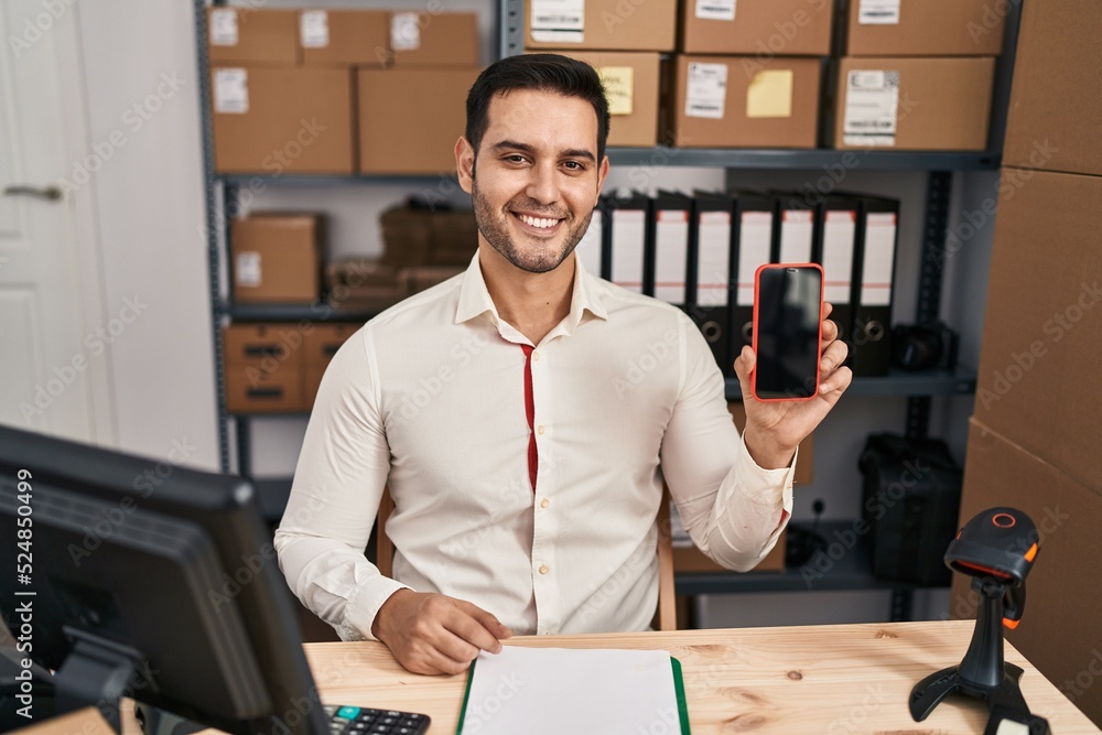 Young hispanic man with beard working at small business ecommerce showing smartphone screen looking positive and happy standing and smiling with a confident smile showing teeth Young hispanic man with beard working at small business ecommerce showing smartphone screen looking positive and happy standing and smiling with a confident smile showing teeth