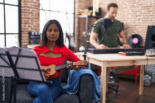 Fotografie Young indian woman playing ukulele at music studio thinking attitude and sober e