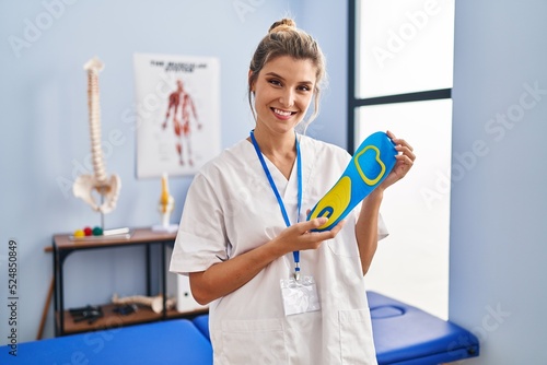 Young woman holding shoe insole at physiotherapy clinic smiling with a happy and cool smile on face. showing teeth. photo