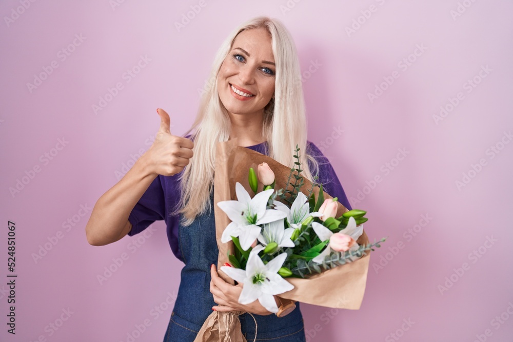 Caucasian woman holding bouquet of white flowers doing happy thumbs up gesture with hand. approving expression looking at the camera showing success. Caucasian woman holding bouquet of white flowers doing happy thumbs up gesture with hand. approving expression looking at the camera showing success.