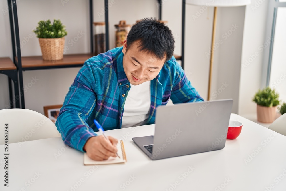 Young chinese man using laptop writing on notebook at home Young chinese man using laptop writing on notebook at home
