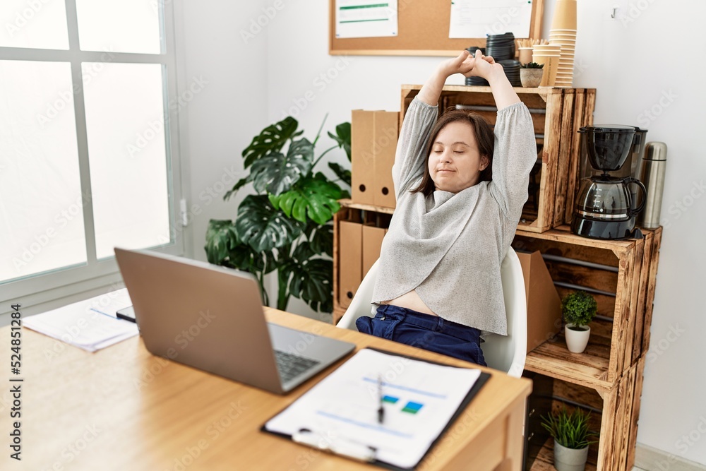 Brunette woman with down syndrome stretching arms relaxing at business office Brunette woman with down syndrome stretching arms relaxing at business office