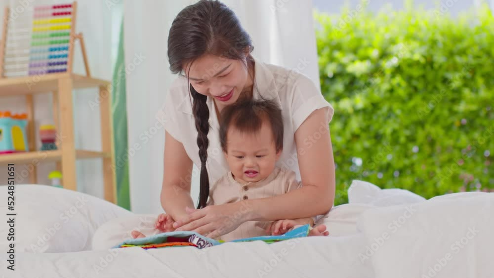 Happy asian young mother smile reading fairy tale story with adorable baby boy spending time at home. infant baby enjoy with fairy tale story from mom on bed looking book together. Baby care concept Happy asian young mother smile reading fairy tale story with adorable baby boy spending time at home. infant baby enjoy with fairy tale story from mom on bed looking book together. Baby care concept