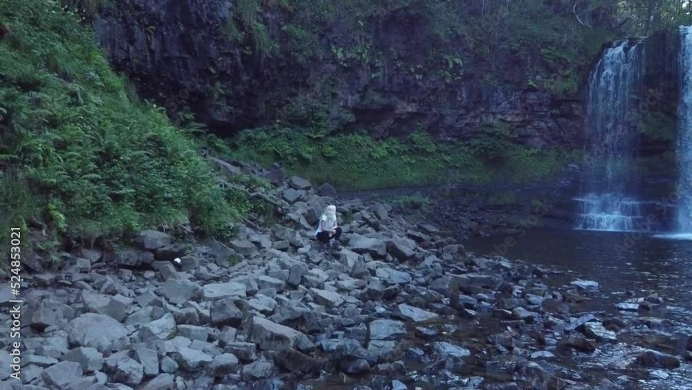 girl sitting on rocks next to a large waterfall in Wales girl sitting on rocks next to a large waterfall in Wales