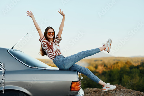 A woman with a car stopped on the road to rest on the journey raised her arms and legs from happiness and a beautiful landscape