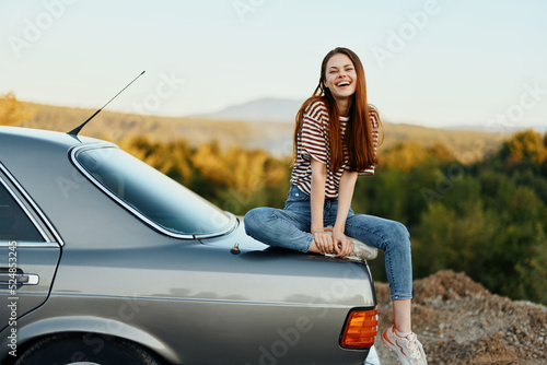 A woman car driver sits on the trunk of a car and smiles admiring a beautiful view of autumn nature and mountains © SHOTPRIME STUDIO