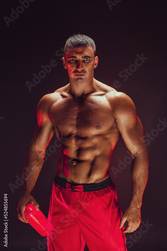 Fototapeta Muscular man with protein drink in shaker over black background