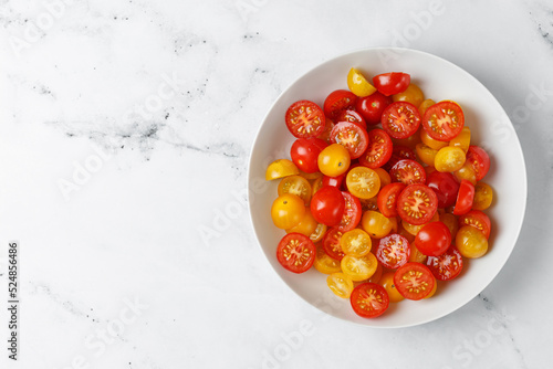 Diet and healthy salad with cherry red and yellow tomatoes, olive oil on white plate and marble background. Keto diet, healthy food. Fresh salad bowl.