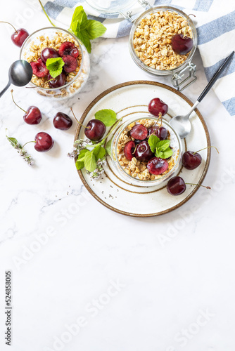 Healthy menu concept. Home made granola breakfast. Glass of parfait made of granola, berries cherry, yogurt with chia seeds on rustic table. View from above. Copy space.