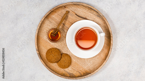 A cup of tea and coockies and honey on a wooden tray. View from above.