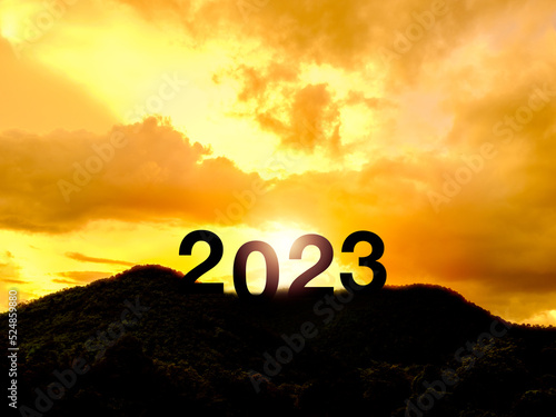 Happy New year 2023 with large silhouette letters on the mountain with beautiful sunset light, sunlight, golden sky and clouds for success concept. Welcome Merry Christmas and Happy New Year in 2023.