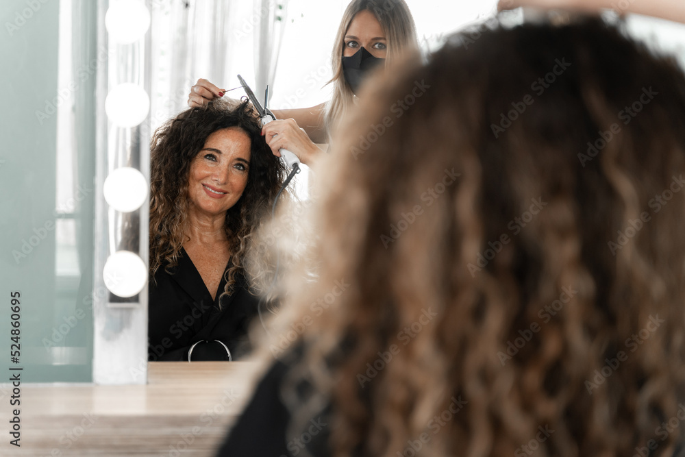 Reflection on the mirror of a hairdresser curling the hair of a customer Reflection on the mirror of a hairdresser curling the hair of a customer