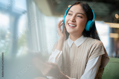 relax joyful casual asian female adult woman casual cloth enjoy listening music from streaming online playing music playlist application on smartphone via earphone  on sofa couch at co working space