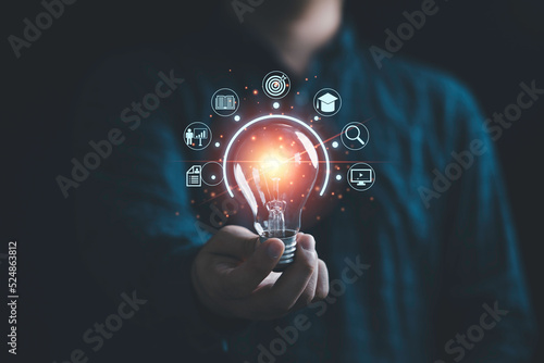 Businessman holding glowing lightbulb with learning icons for study knowledge to creative thinking idea and problem solving solution concept. photo