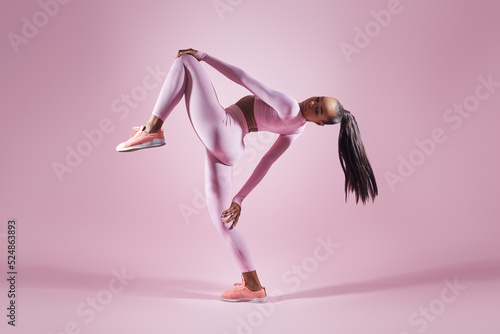 Attractive young woman in sports clothing doing stretching exercises against pink background
