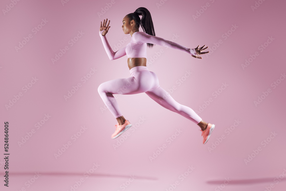 Confident young woman in sports clothing jumping against pink background