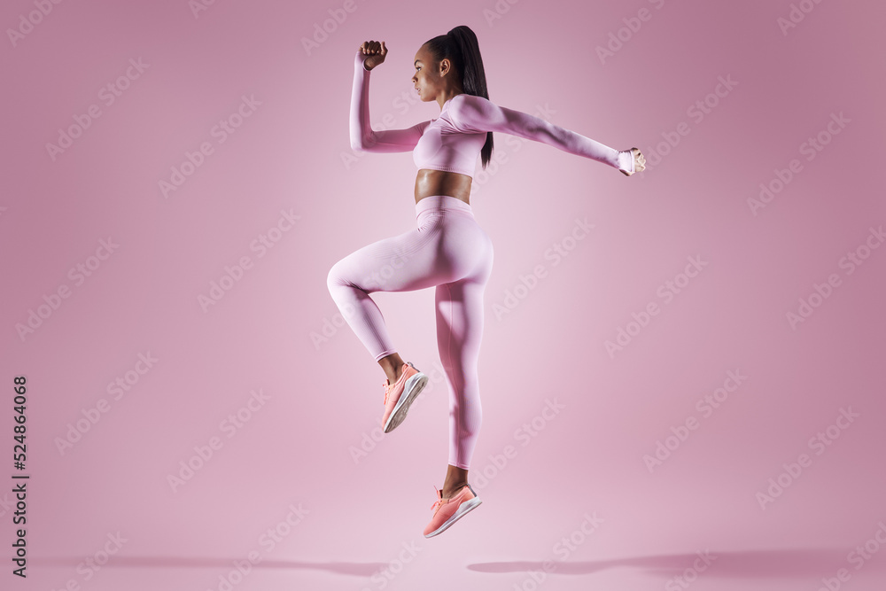 Confident young woman in sports clothing jumping against pink background