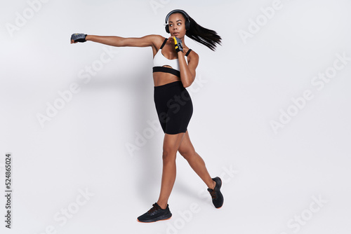 Фотография Confident young African woman in sports clothing practicing in punching against