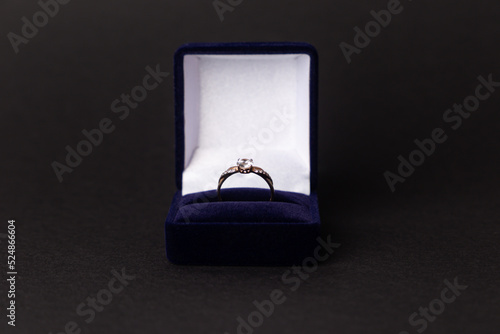 Jewelry, gold diamond ring in a blue box on a black background, isolated.  A ring for a marriage proposal. Close-up. Front view. A place for your text.