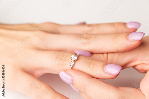 The concept of engagement, loyalty. The girl puts a diamond ring on her finger. Manicure, soft purple nails. Close-up. A place for your text.