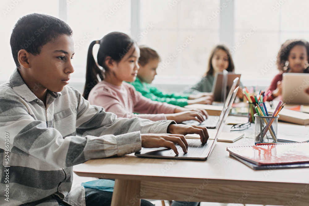 Side View Of African American Schoolboy Using Laptop In Classroom Side View Of African American Schoolboy Using Laptop In Classroom